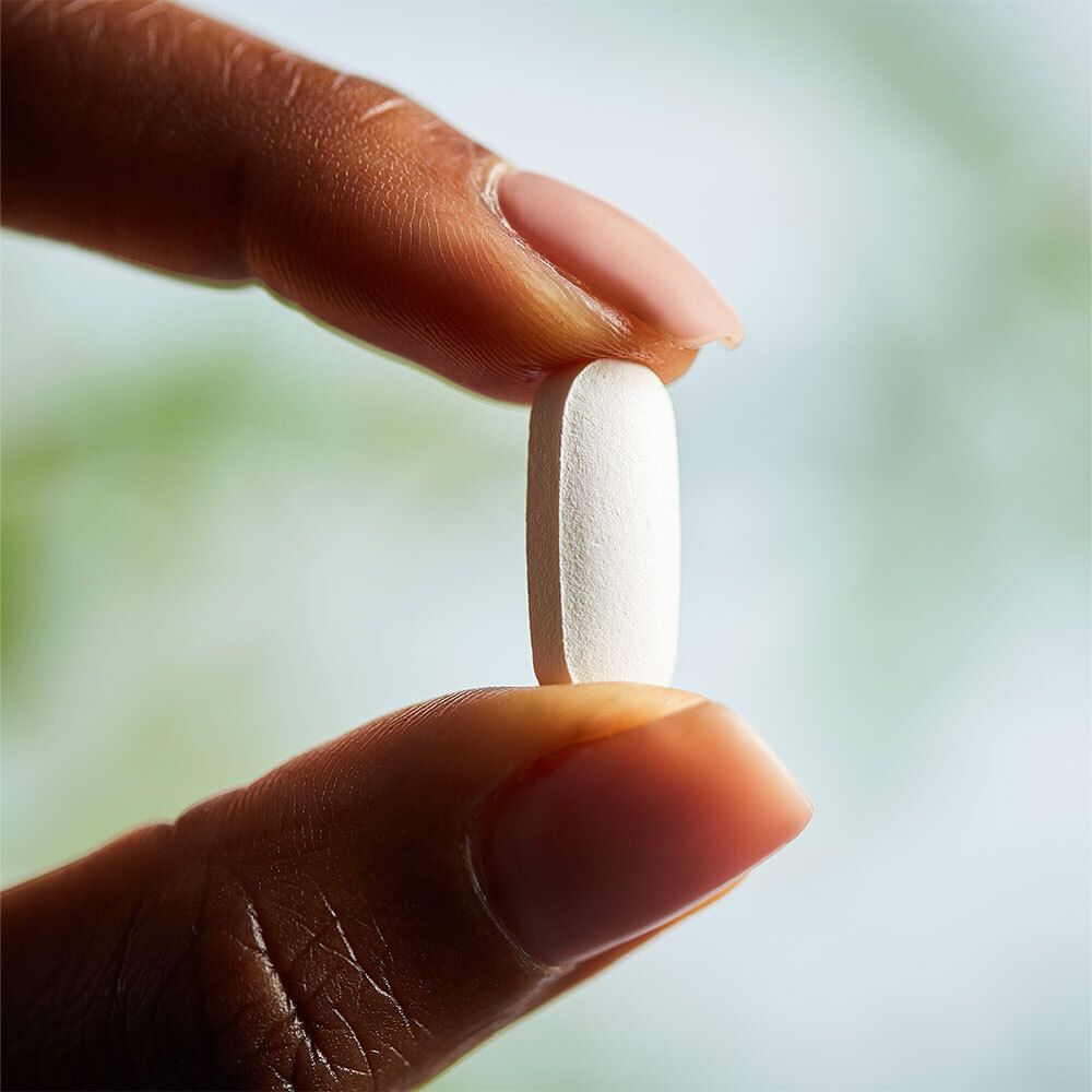 Un comprimé ovale blanc tenu entre les doigts. Gros plan.