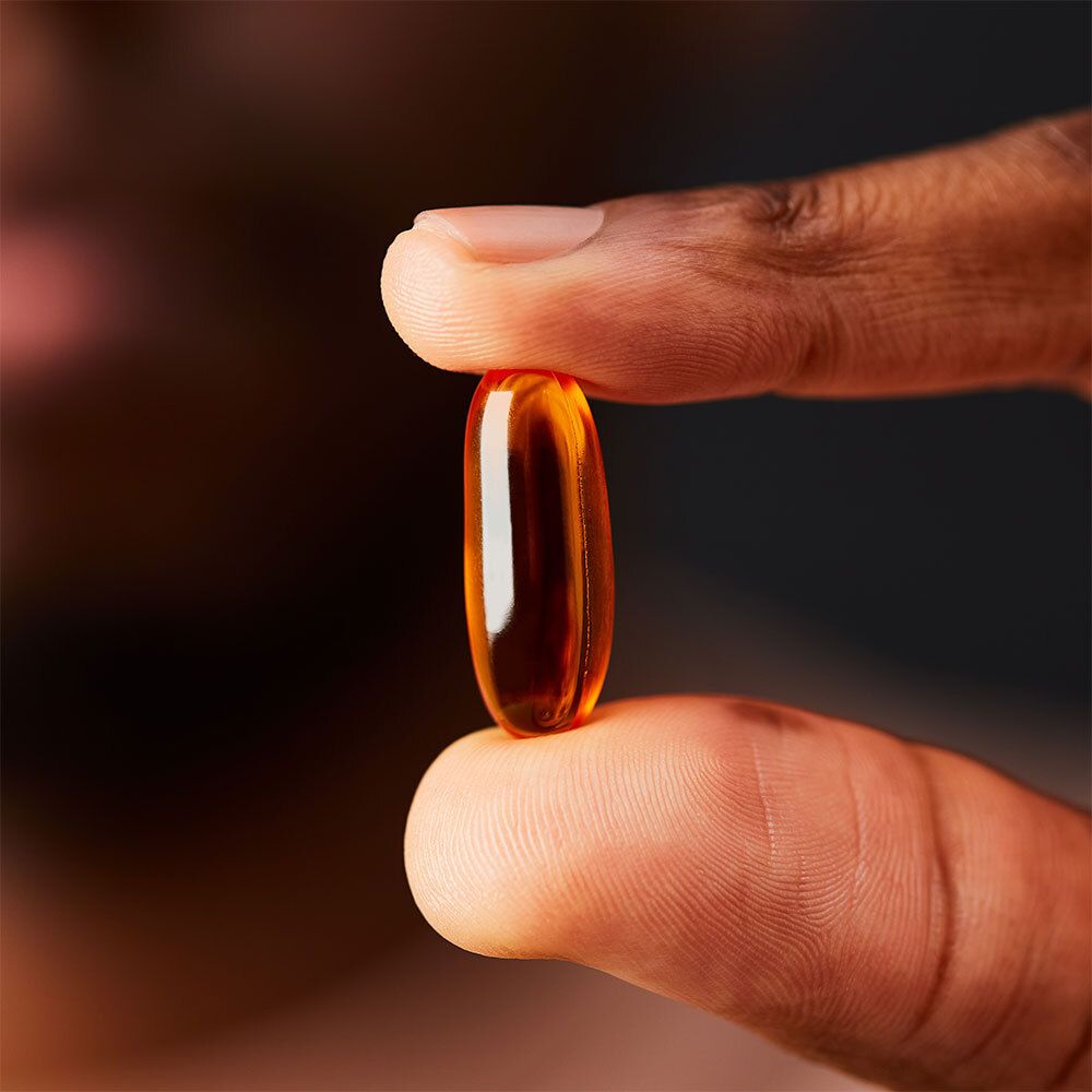 Gélule jaune tenue entre deux doigts. Couleur de peau.