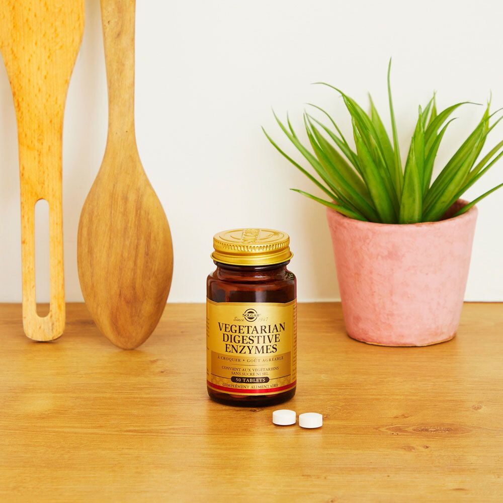 Flacon brun avec deux comprimés à côté. Sur une table en bois, près d'ustensiles de cuisine et d'une plante.