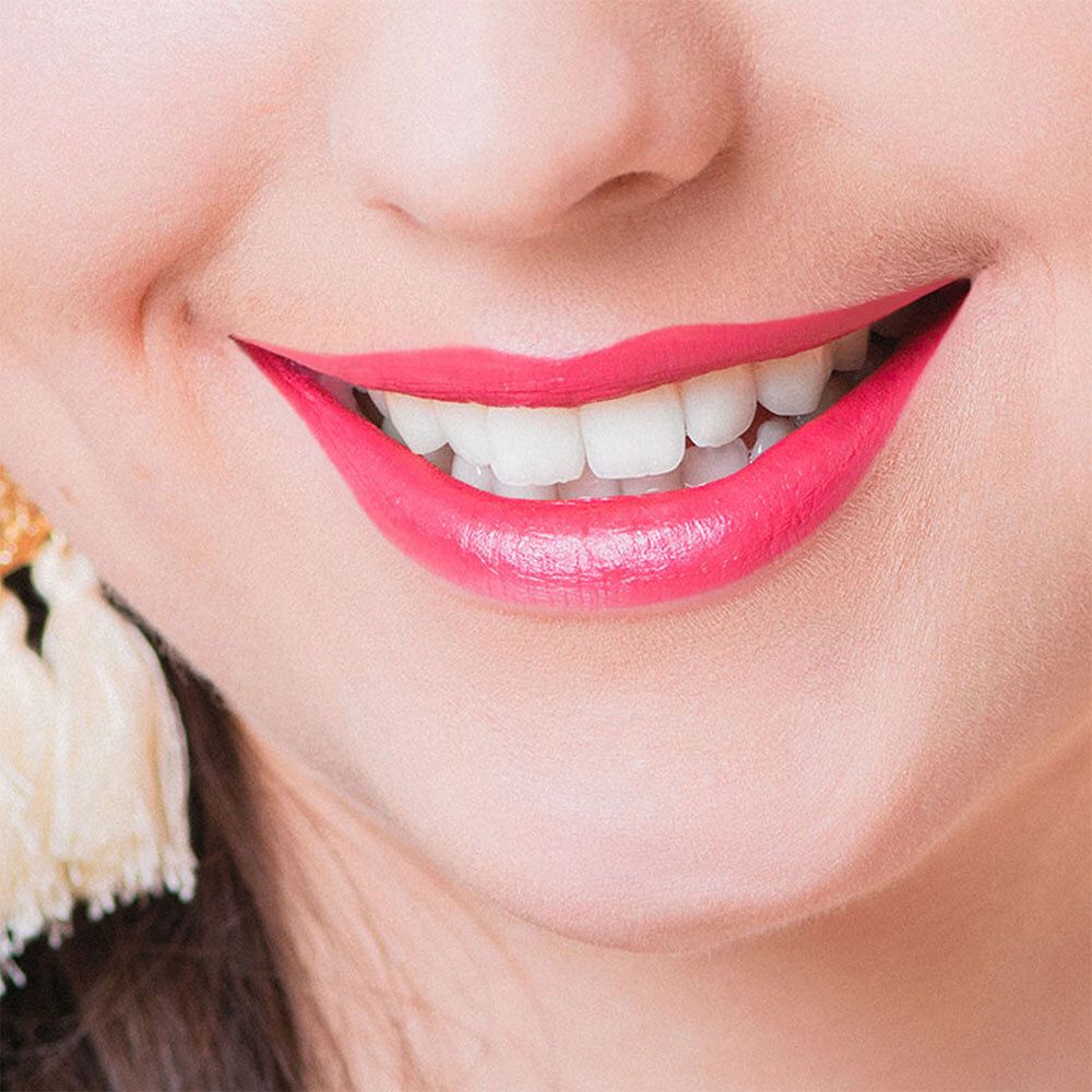 Gros plan d'une bouche souriante avec du rouge à lèvres rose. Dents blanches visibles.