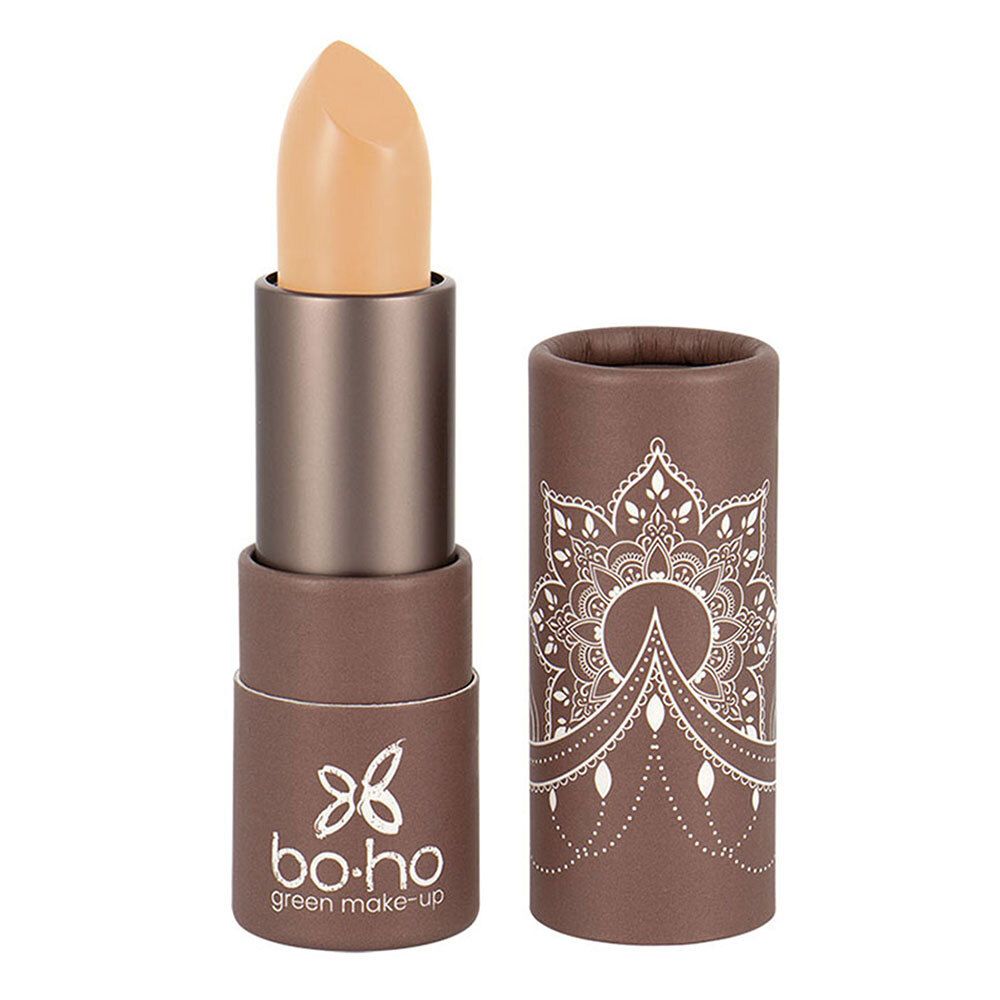 Correcteur beige en bâton, partiellement sorti de son étui. Étui marron avec motif blanc et logo.