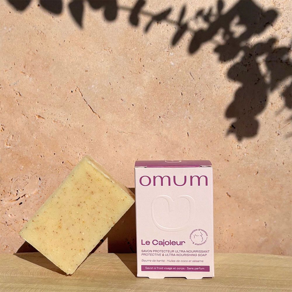 Savon OMUM Le Cajoleur et emballage devant un fond texturé.