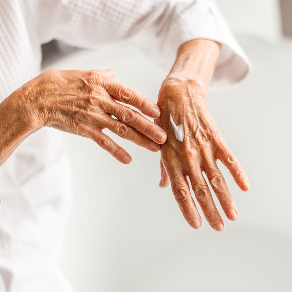 Mains âgées appliquant de la crème. Une petite quantité de crème sur la paume. La personne porte un peignoir blanc.
