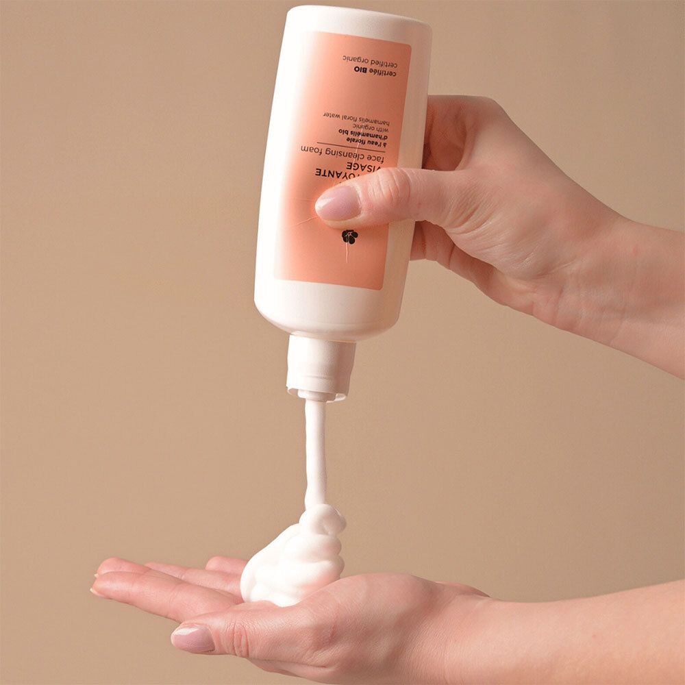 Main pressant la mousse nettoyante visage Avril hors d'un flacon dans la paume.