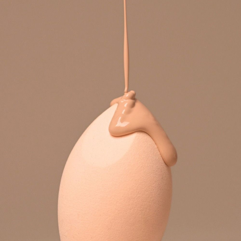 Éponge de maquillage beige, forme goutte. Du maquillage liquide est versé sur la surface.