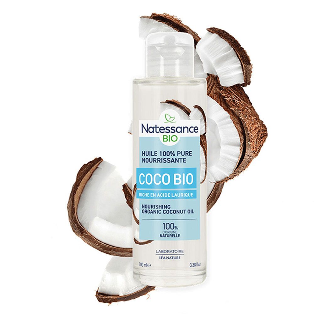 Flacon en verre avec bouchon argenté, entouré d'éclats de noix de coco. Étiquette Natessance Coco Bio et texte.