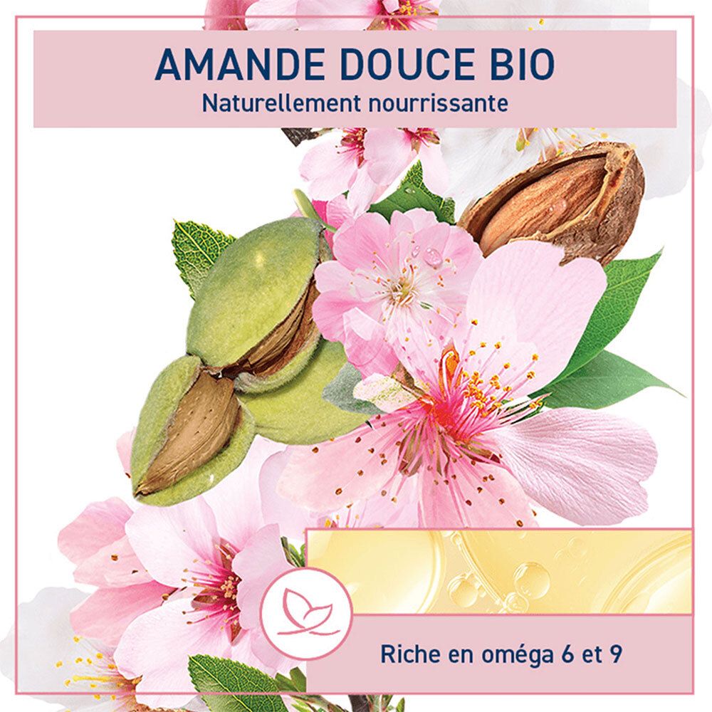 Étiquette rose avec nom et logo du produit, entourée de fleurs et d'amandes. Liquide jaunâtre.