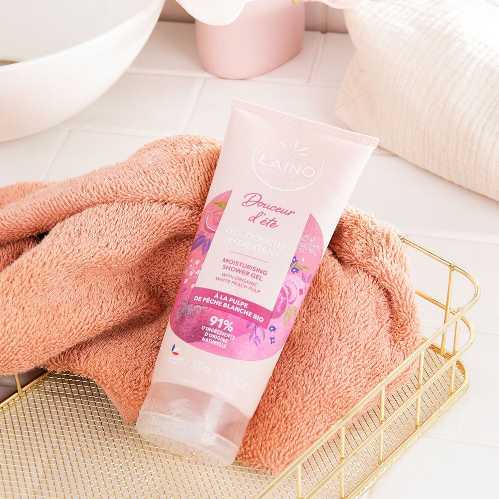 Tube rose LAINO "Gel Douche Hydratant" sur une serviette et dans un panier. Fond: salle de bain.