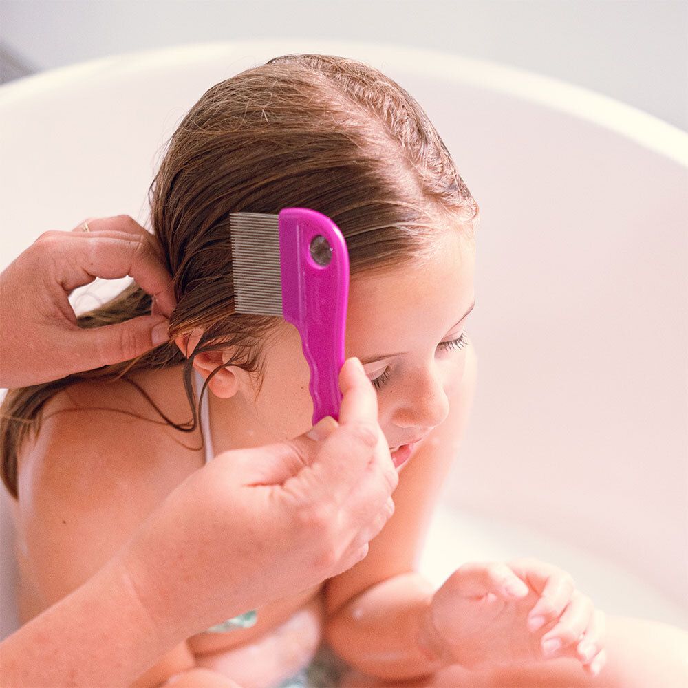Fille dans une baignoire, on lui peigne les cheveux avec un peigne rose.