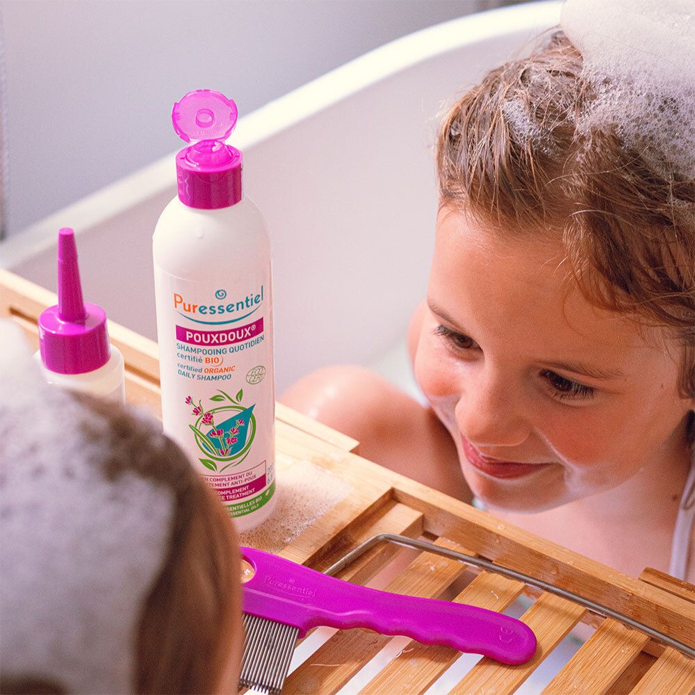 Fille dans une baignoire avec de la mousse. À côté, shampoing et peigne.