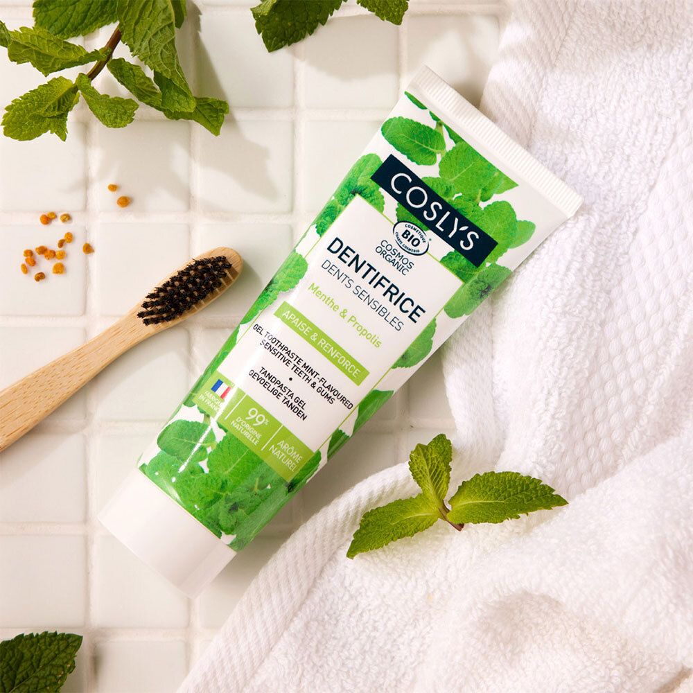 Tube de dentifrice avec brosse à dents et feuilles. Inscription: COSLYS, Dents Sensibles. Sur serviette blanche.