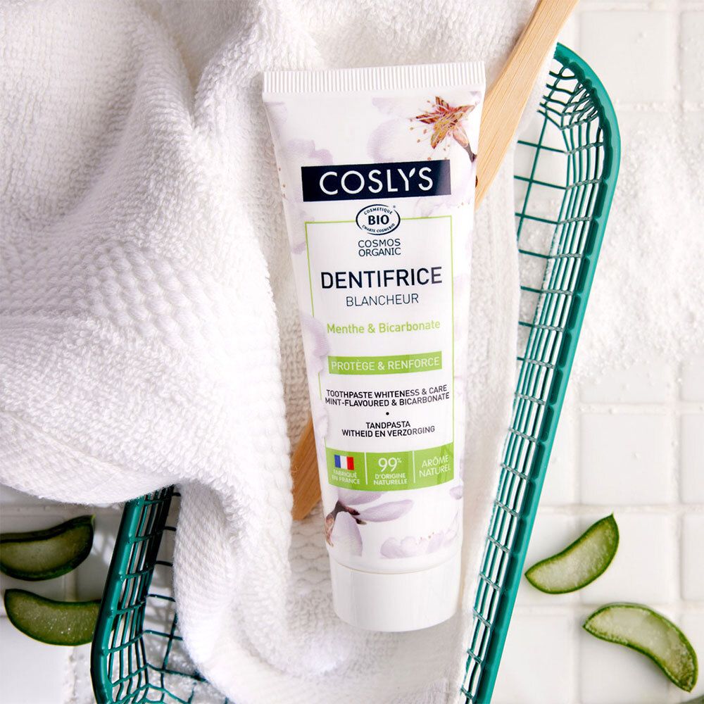 Tube de dentifrice Coslys, Menthe & Bicarbonate, près d'une serviette, brosse à dents et panier. Certification bio.