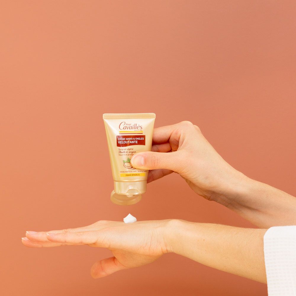 Tube de crème pour les mains pressée dans une main. La crème est appliquée sur la paume. Fond orange.