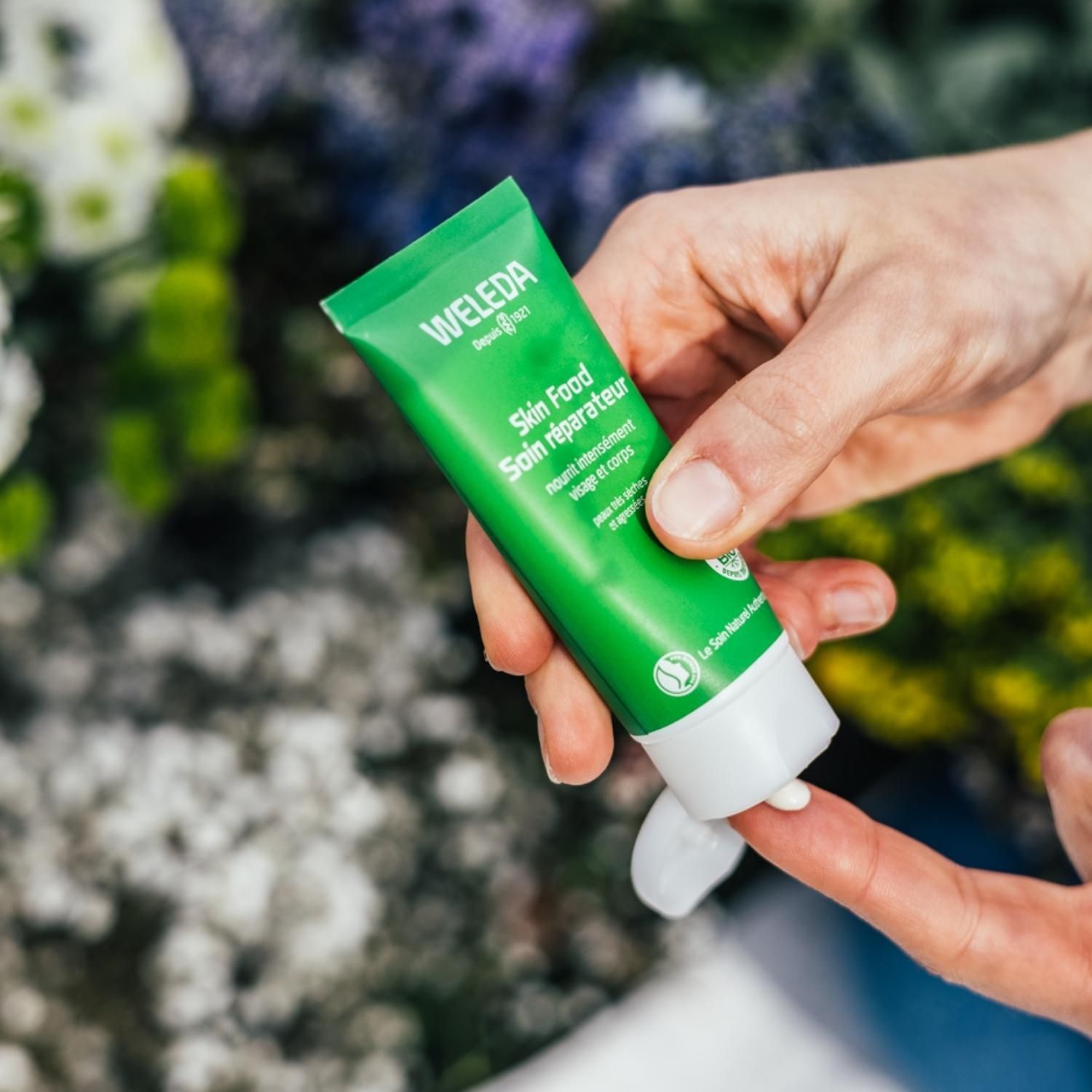 Tube vert Weleda Skin Food. Produit appliqué sur un doigt. Texte : Soin réparateur.