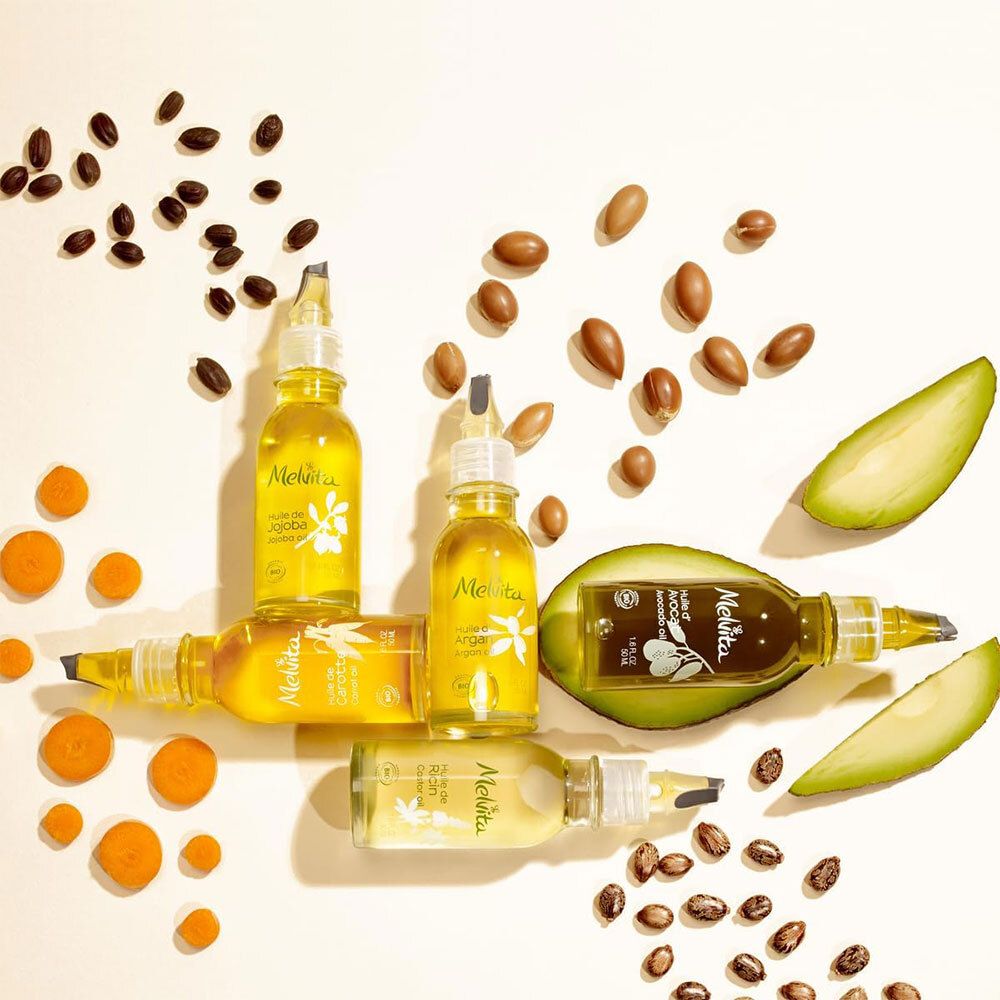Plusieurs flacons de liquide jaune, entourés de graines et de fruits. Inscription Melvita.