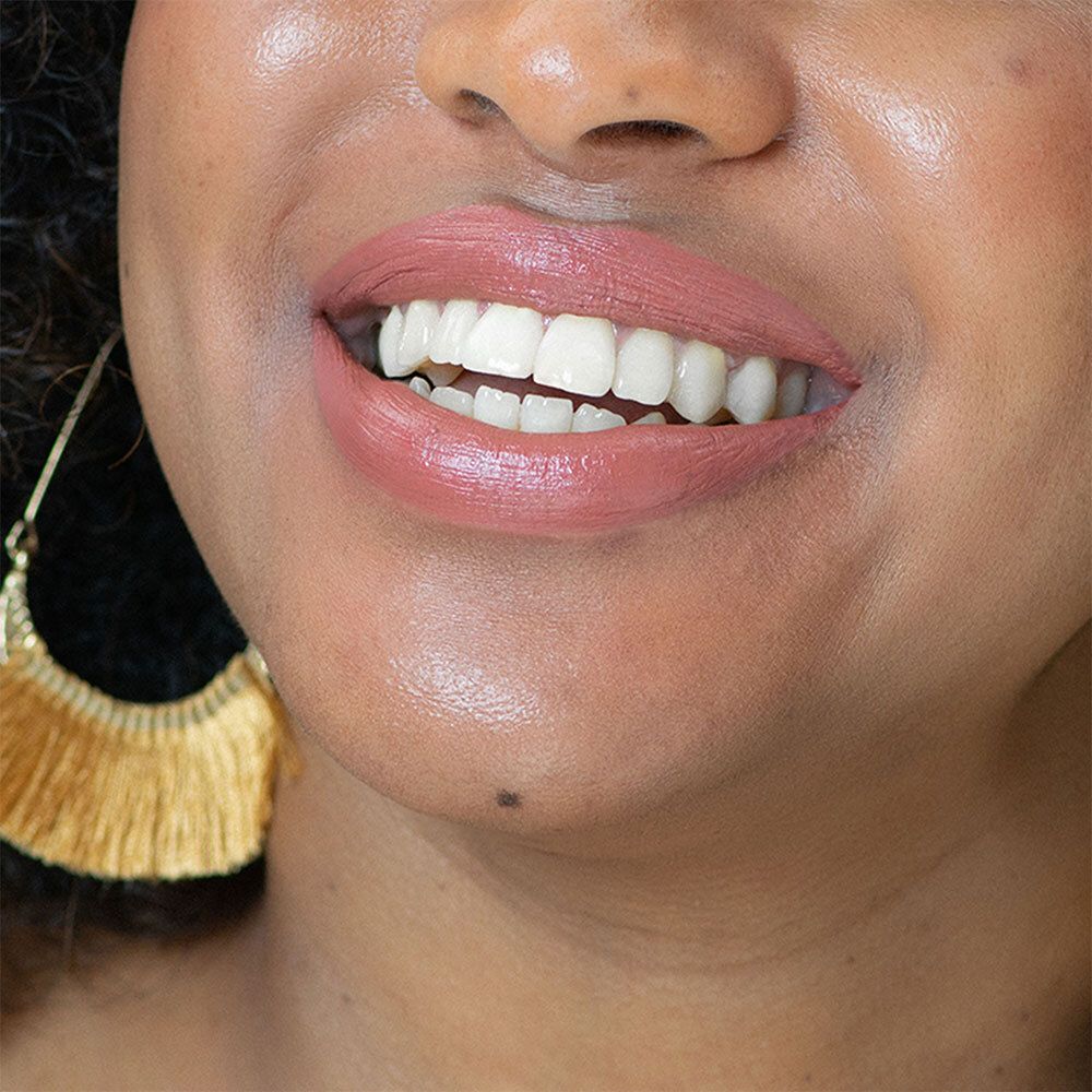 Gros plan sur des lèvres avec du rouge à lèvres rose. Boucles d'oreilles dorées. Peau brillante.