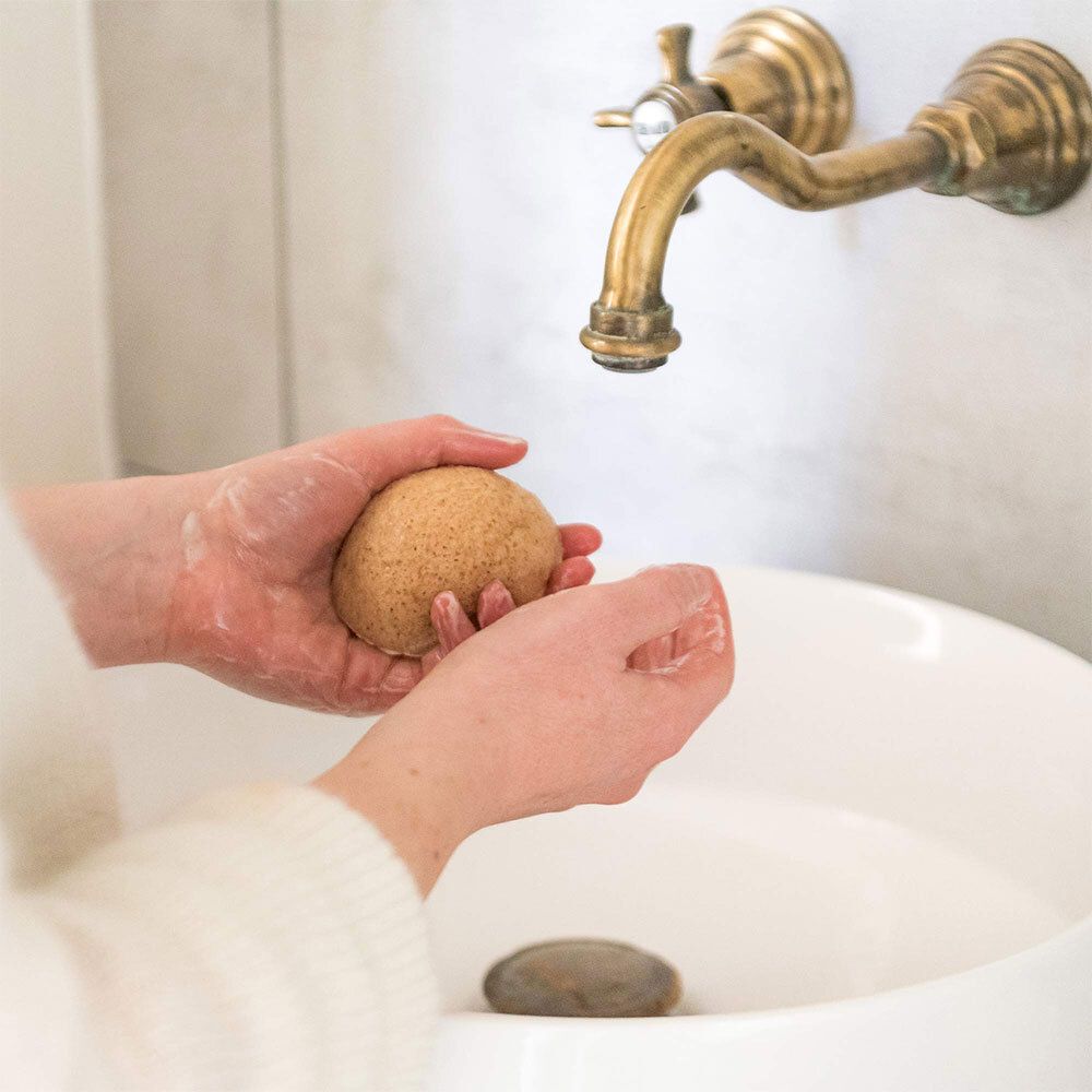 Mains tenant une éponge Konjac mouillée au-dessus d'un lavabo.