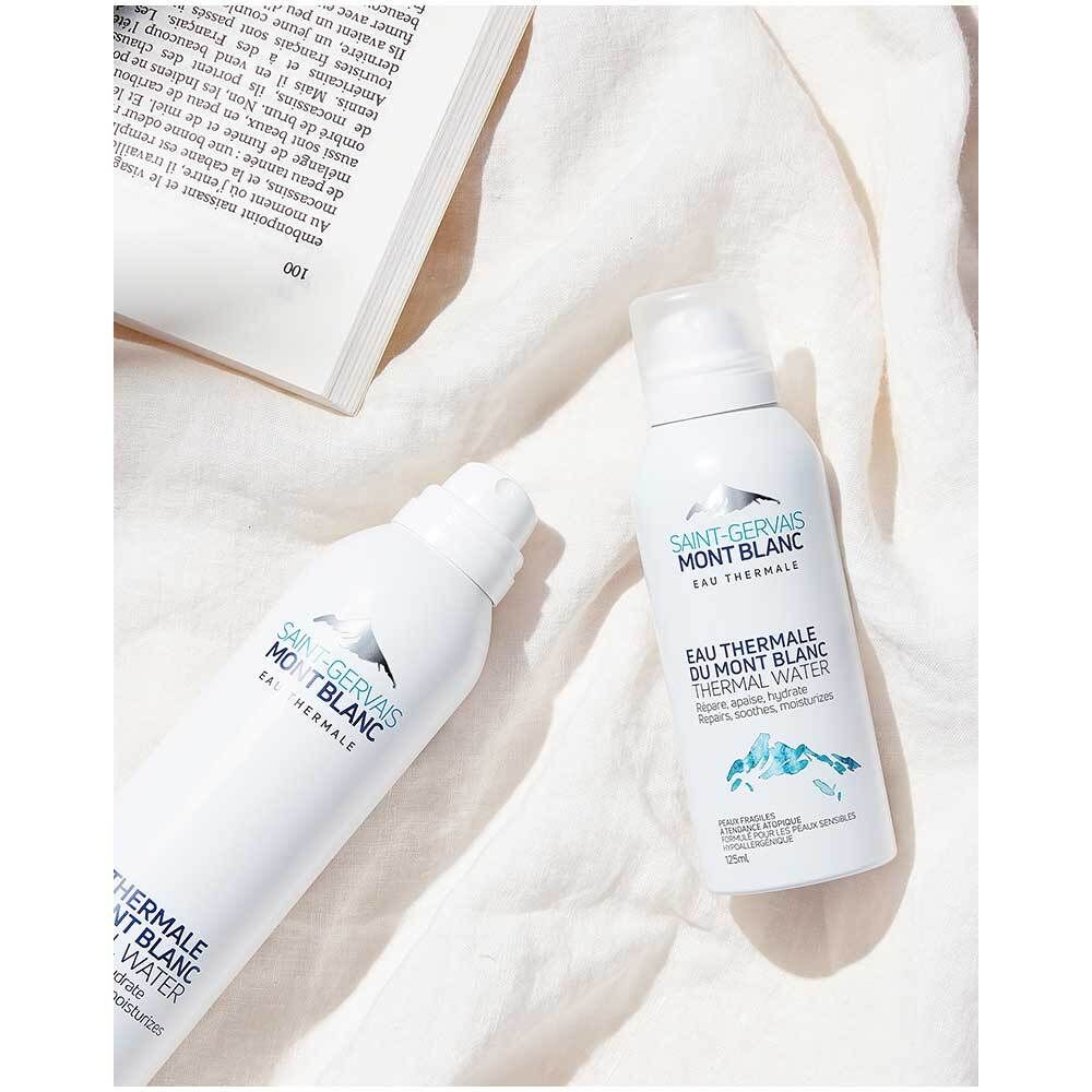 Deux sprays blancs avec logo SAINT-GERVAIS MONT BLANC. Sur tissu blanc. Un livre en arrière-plan.