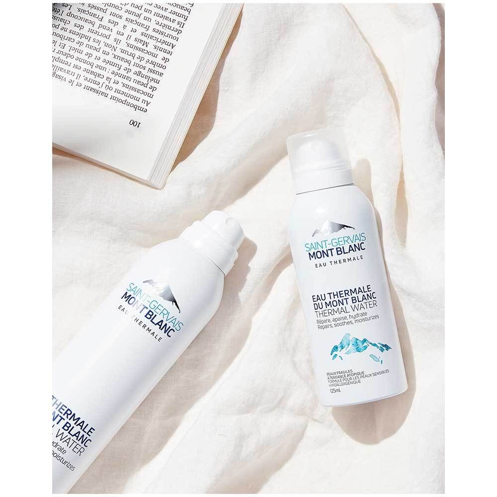 Deux flacons spray blancs avec texte bleu. Nom du produit: Saint Gervais MONT BLANC Thermalwasser. Sur tissu blanc.