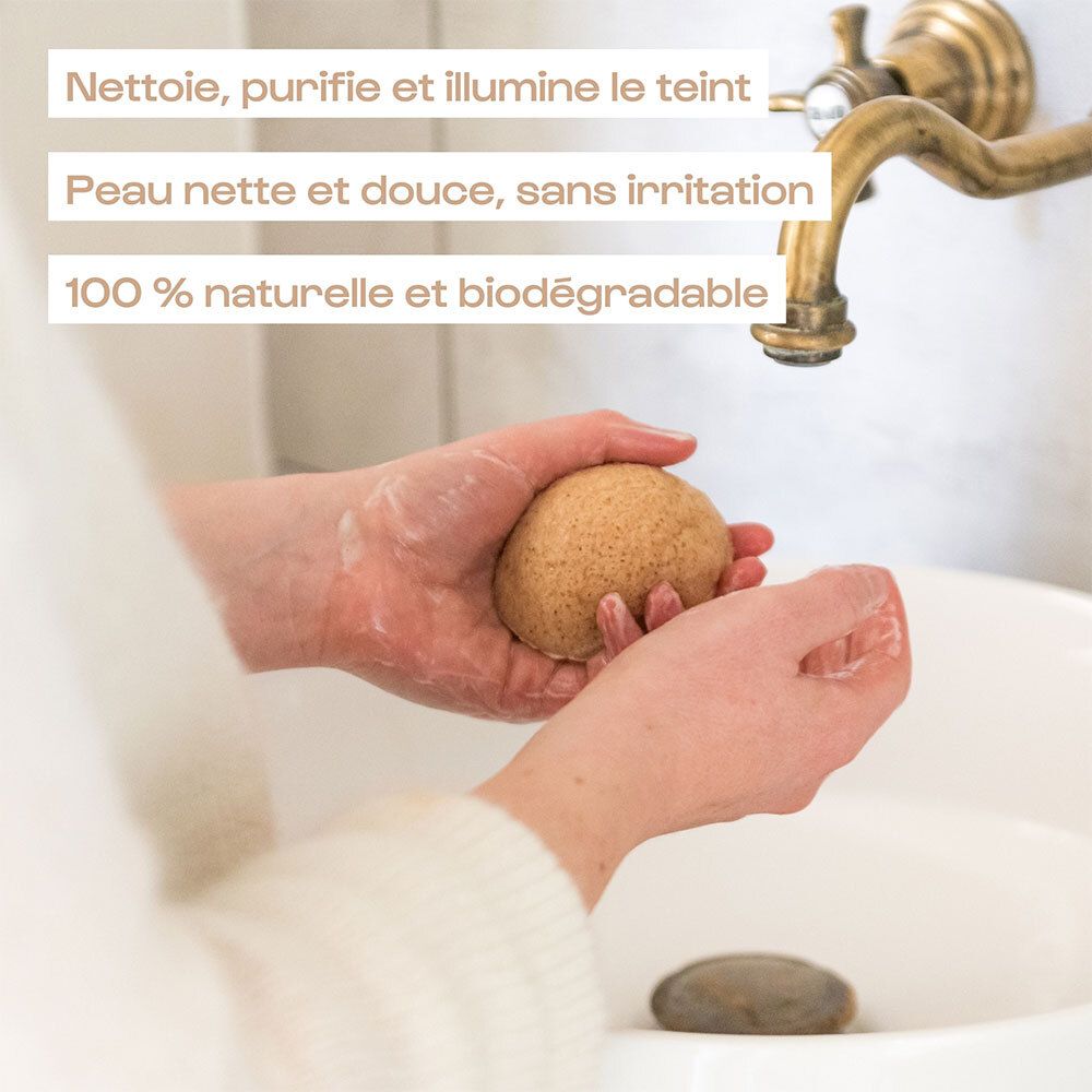 Mains utilisant une éponge konjac OMUM sous l'eau courante dans un lavabo.