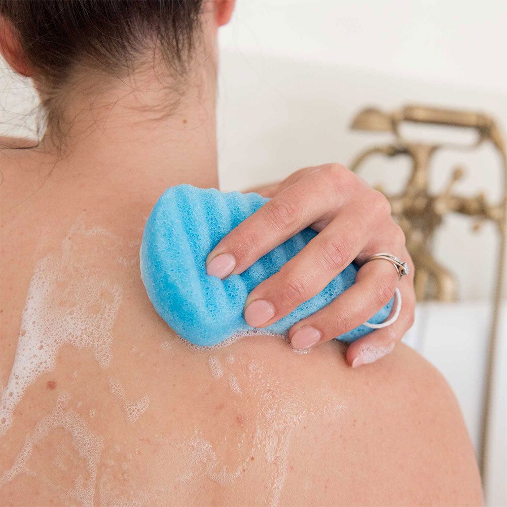 Femme utilisant une éponge konjac bleue pour exfolier doucement son dos.