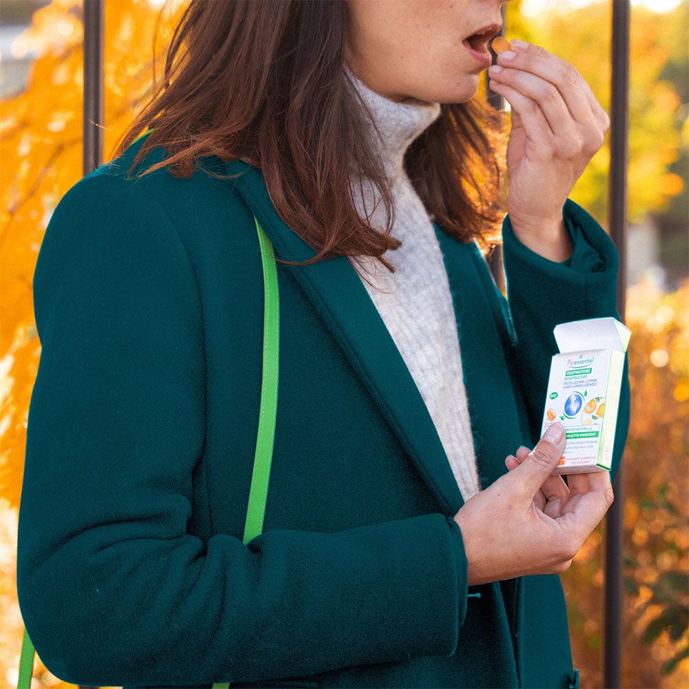 Personne tenant une boîte de pastilles PURESSENTIEL RESPIRATOIRE. Vert, blanc, jaune. Femme en veste verte. En extérieur.