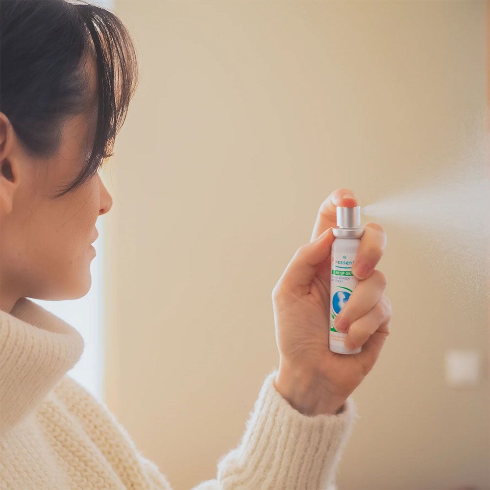 Personne vaporisant le spray Resp'OK Air de Puresseentiel. Spray blanc. Bouchon vert. Mur beige.
