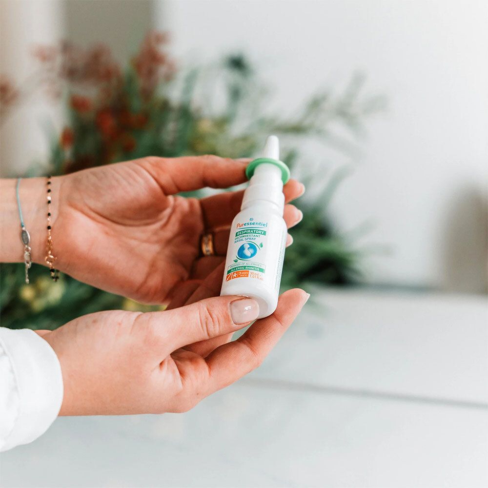 Flacon de spray nasal blanc avec anneau vert. Mains tenant le flacon. Inscription: Puressentiel Respiratoire.