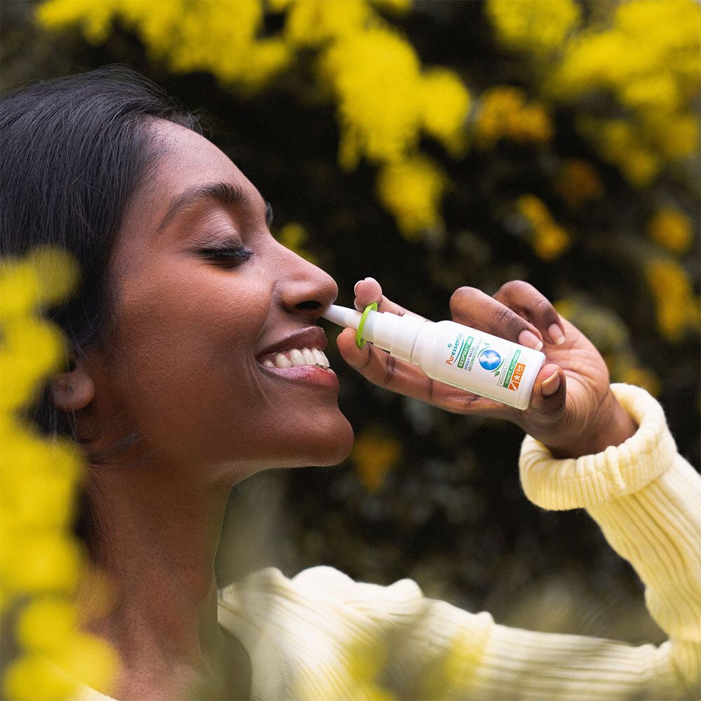 Personne utilisant un spray nasal. Mer de fleurs jaunes en arrière-plan. Inscription: Puressentiel Respiratoire.