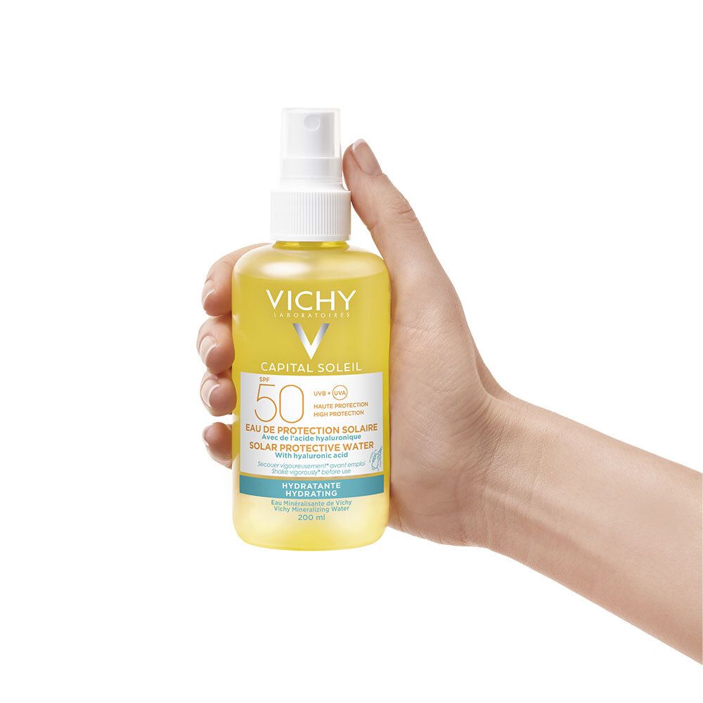Main tenant Vichy Capital Soleil SPF 50. Flacon jaune avec vaporisateur. Étiquette du produit visible.