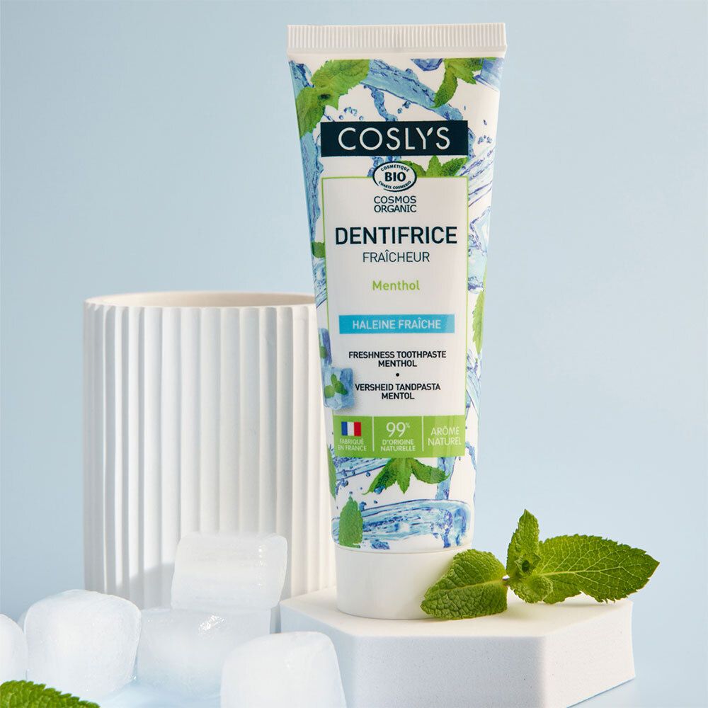 Tube de dentifrice sur socle blanc, entouré de glaçons et de menthe. Nom du produit et mention menthol visibles.