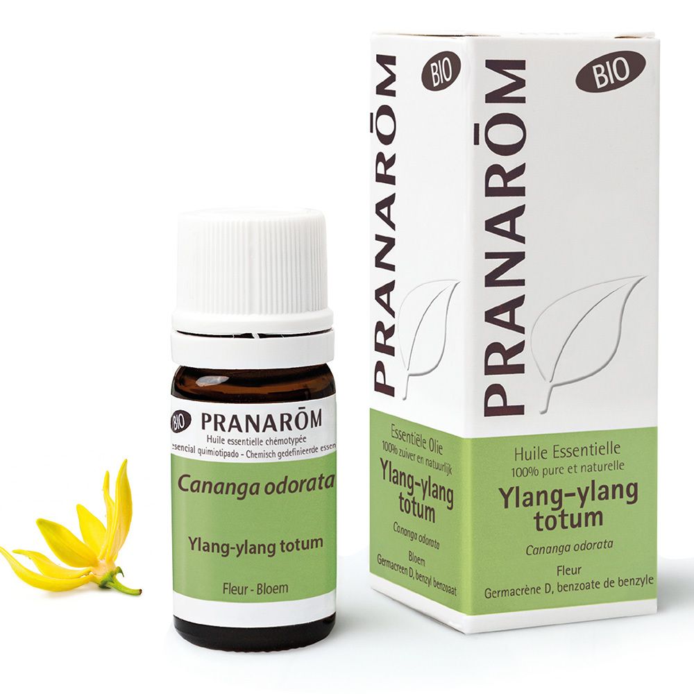 Flacon en verre brun avec bouchon blanc et étiquette. Boîte avec informations produit et fleur jaune à côté.