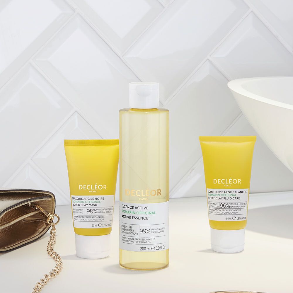 Trois produits sur une surface. Produits: Masque, Essence, Soin Fluide Argile Blanche. Accessoires: sac à main.