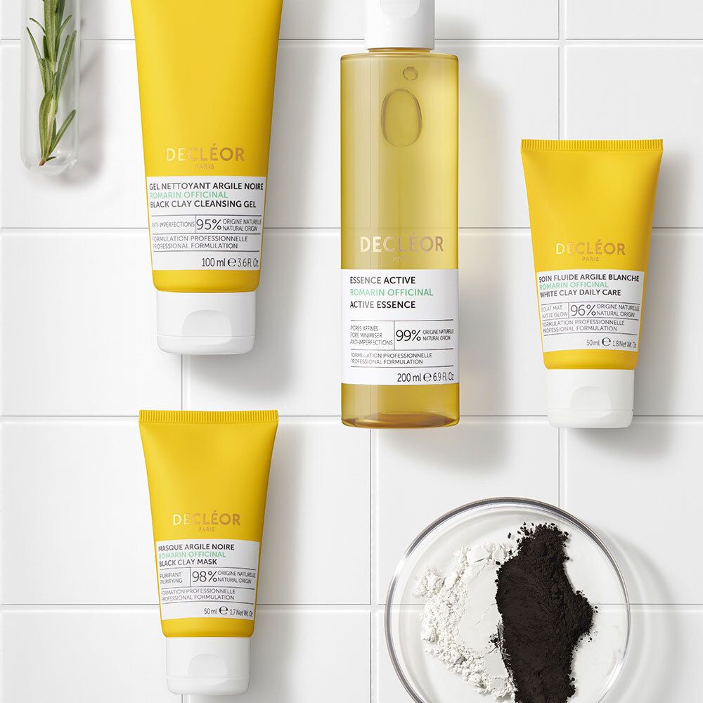 Quatre produits sur une surface. Produits: Gel Nettoyant, Essence Active, Masque Argile Noire, Fluide Argile Blanche.