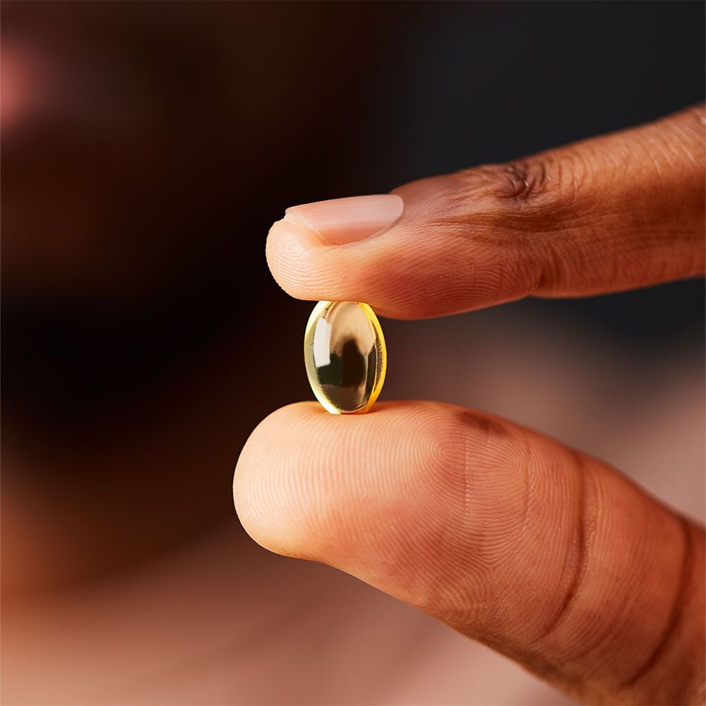 Capsule molle jaunâtre tenue entre deux doigts. Gros plan.