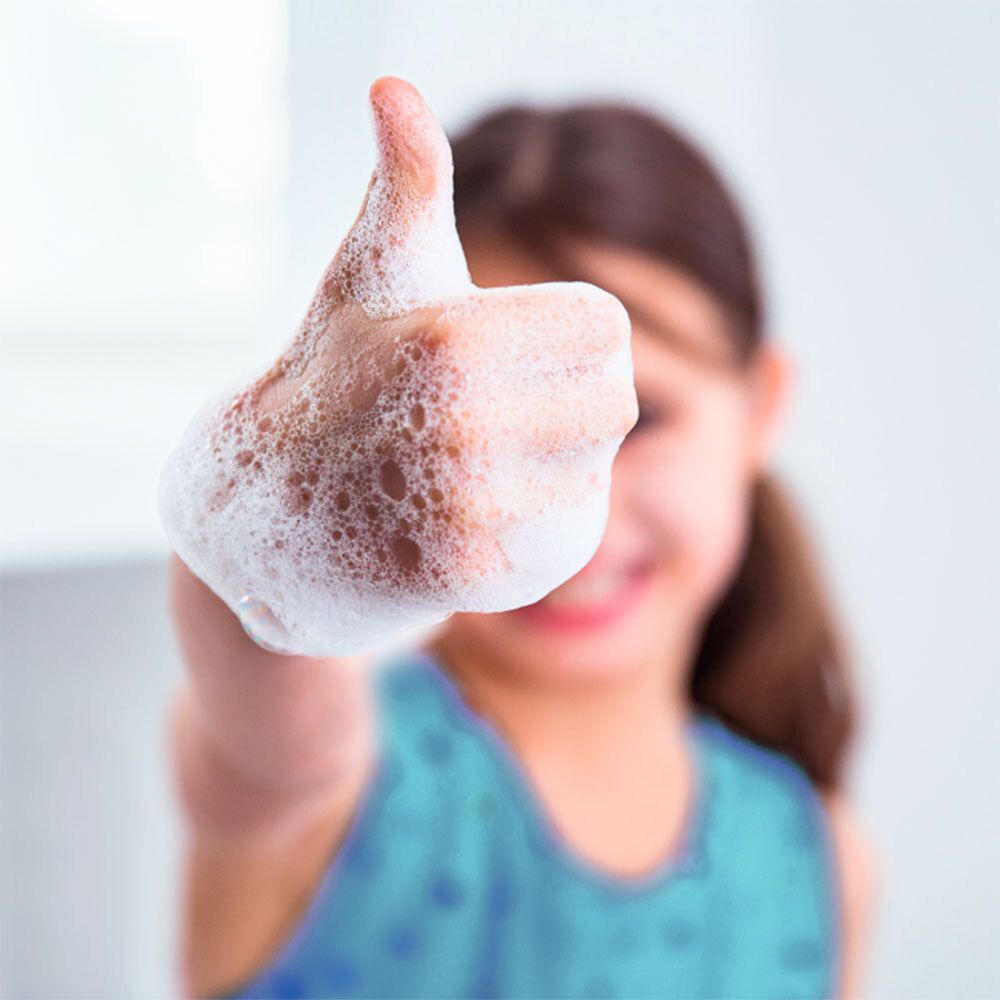 Enfant montrant le pouce en l'air, couvert de mousse de savon. Haut bleu. Visage flou.