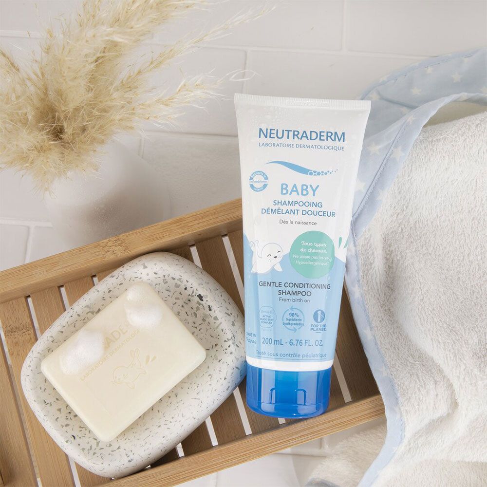 Shampooing Neutraderm Baby sur un plateau, à côté d'un savon et d'une serviette. Inscription: Baby, Shampooing démêlant douceur.