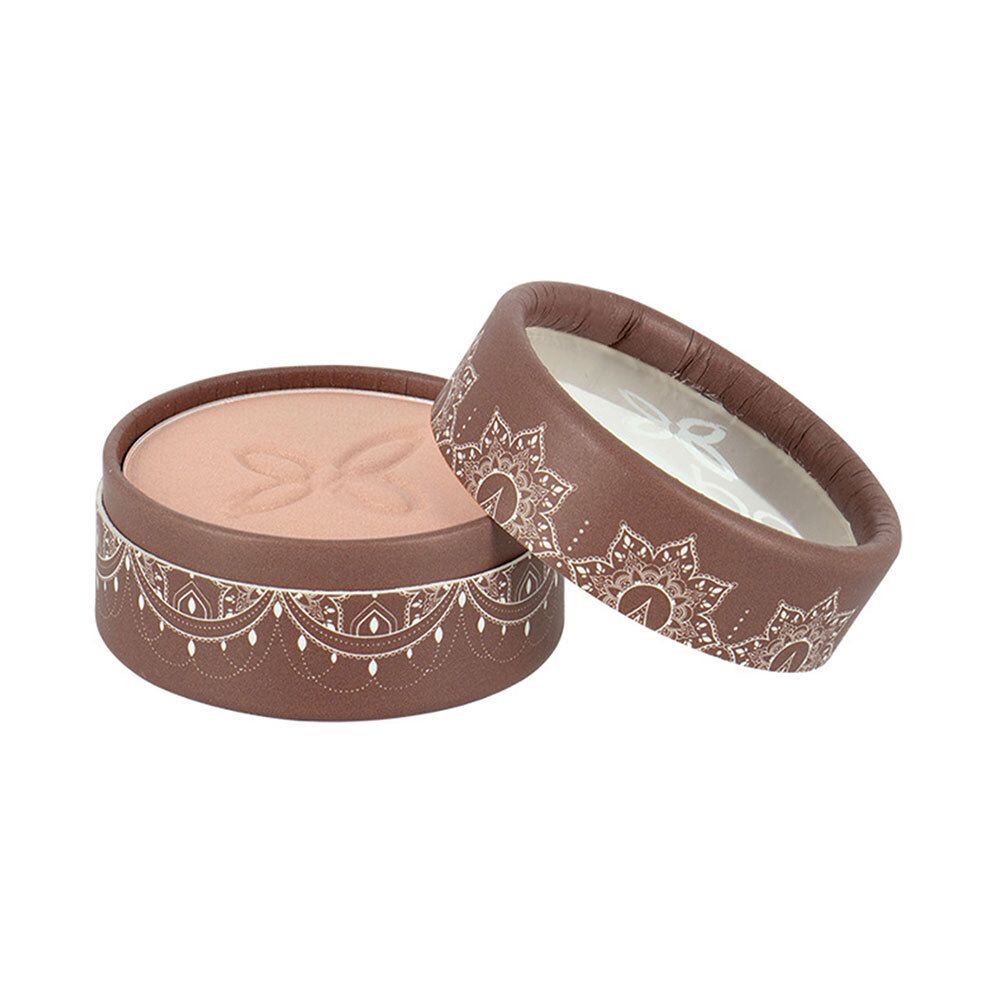 Boîte ronde marron ouverte avec fard à paupières clair. Couvercle avec motif blanc. Nom du produit non visible.