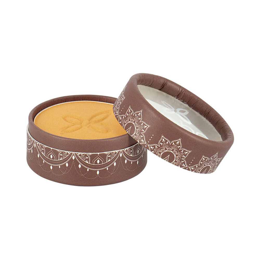 Boîtier rond de fard à paupières doré. Couvercle ouvert, motif floral. Emballage marron avec motif blanc.