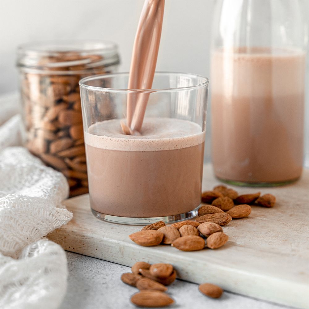 Boisson protéinée au chocolat versée dans un verre, amandes en arrière-plan.