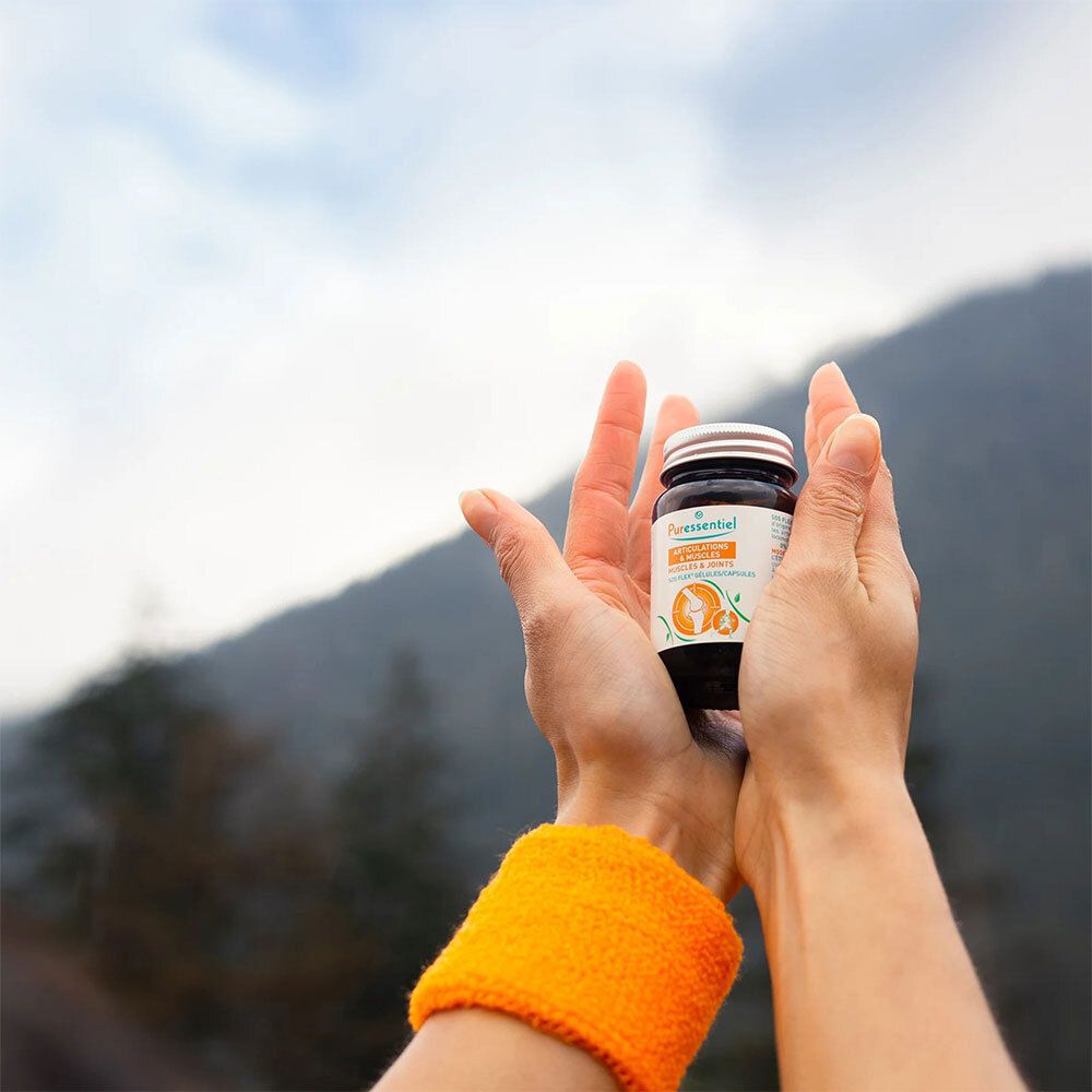 Mains tenant un flacon en verre brun. Articulations & Muscles SOS FLEX® Gélules. Fond : paysage de montagne.