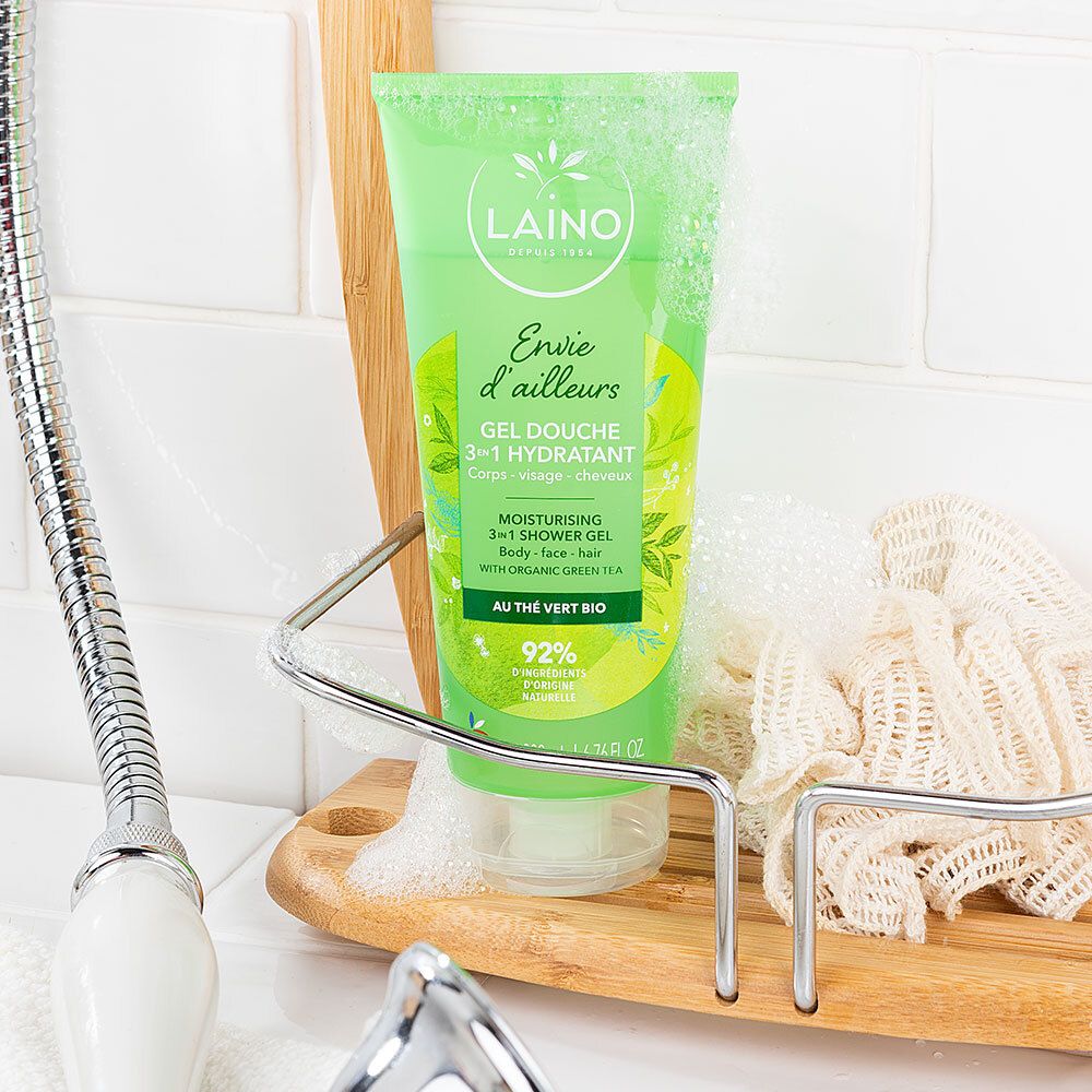 Tube vert avec logo LAINO dans un environnement de douche. À côté du tube, une éponge et de la mousse de savon.