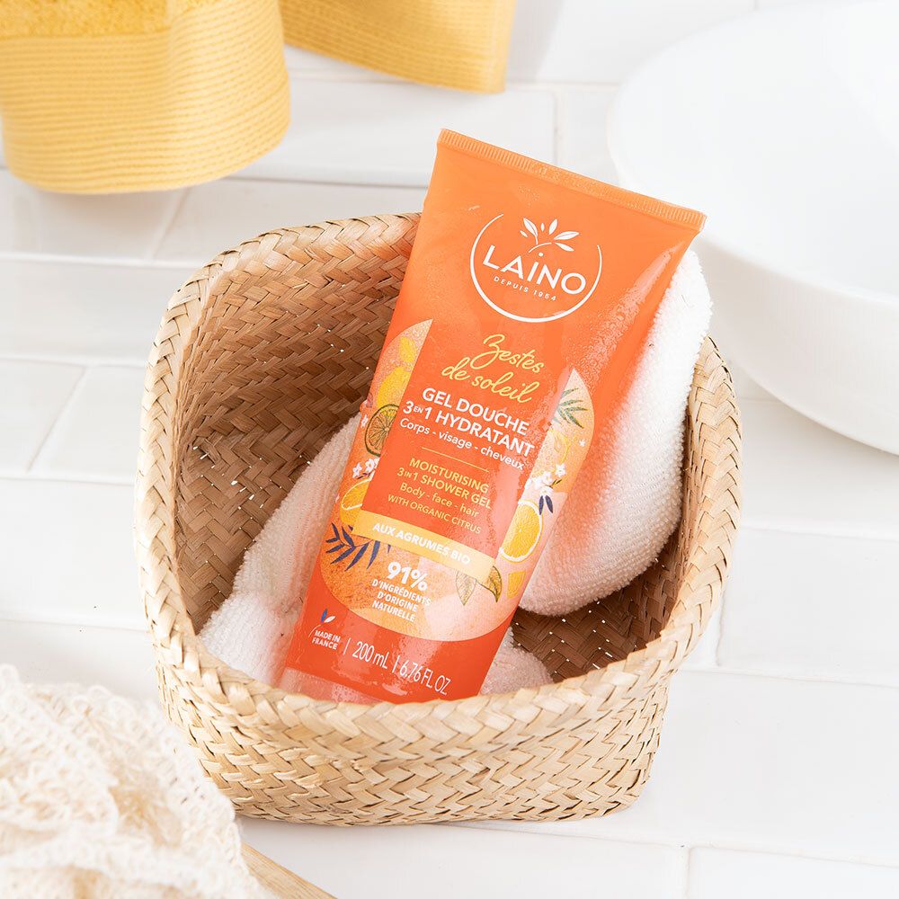 Tube orange dans un panier tressé avec une serviette. Nom du produit et logo clairement visibles. Fond : arrangement de salle de bain.