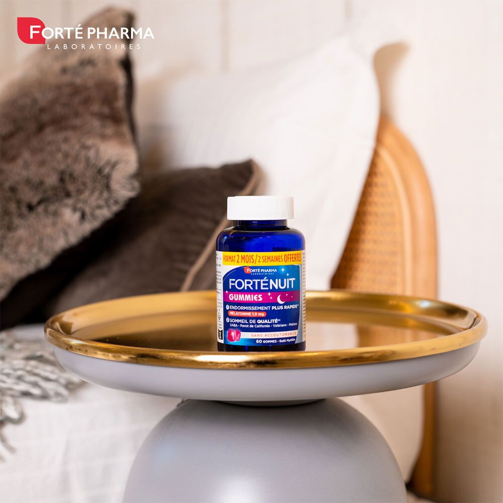 Flacon Forté Nuit Gummies sur un plateau doré. Oreillers et couverture en arrière-plan.