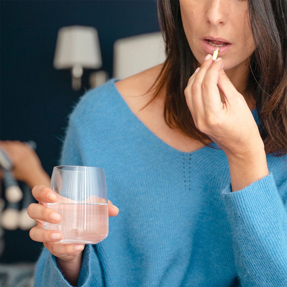 Femme prenant une gélule. Elle tient un verre d'eau. Haut bleu.