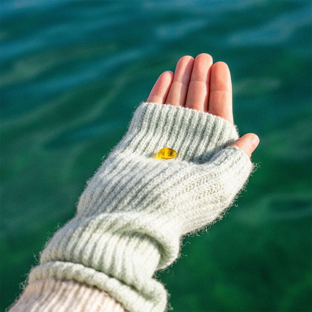 Main avec une pastille jaune dans un gant gris. Fond : eau.