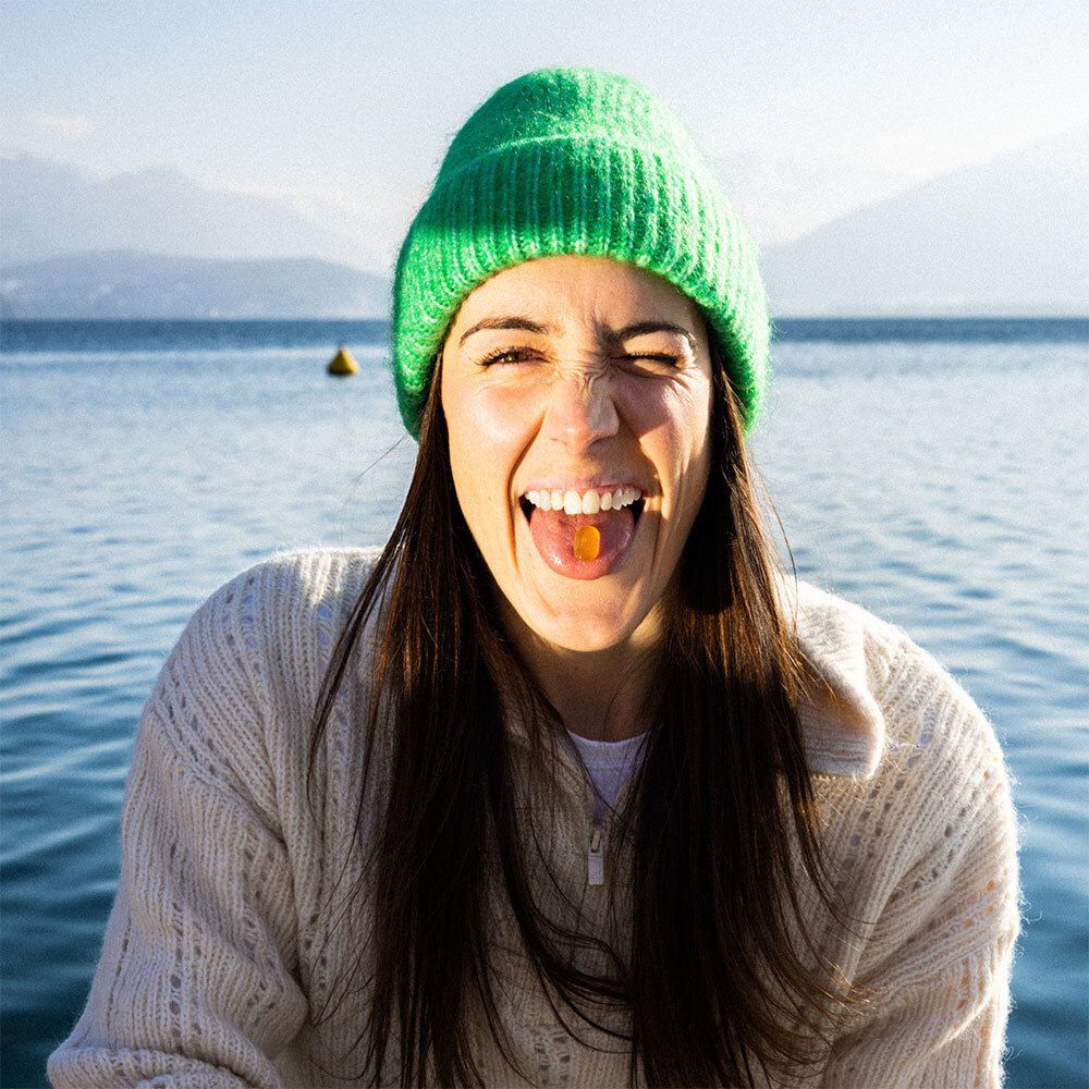 Femme avec bonnet vert, bouche avec pastille jaune. Lac en arrière-plan.