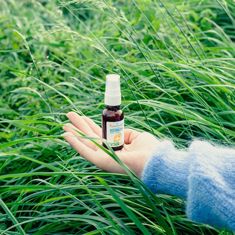 Main tenant Puressentiel AROMA STRESS® Spray Buccal. La main est dans les hautes herbes. L'arrière-plan est flou.