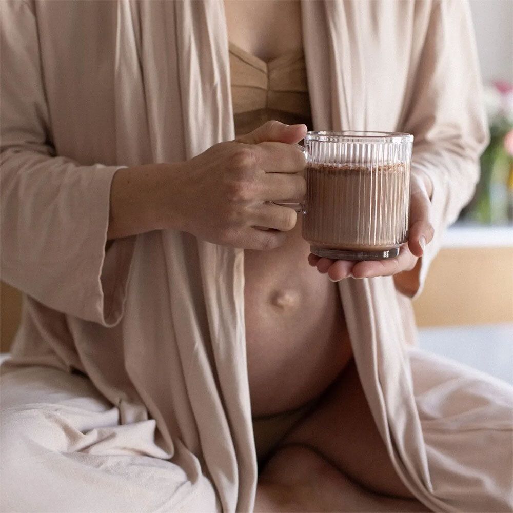 Femme enceinte tenant un verre de boisson. Elle porte un peignoir. Le ventre est visible.