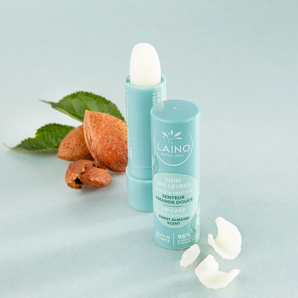 Stick à lèvres et stick ouvert. Étui turquoise, stick blanc. Amandes et feuilles à côté.